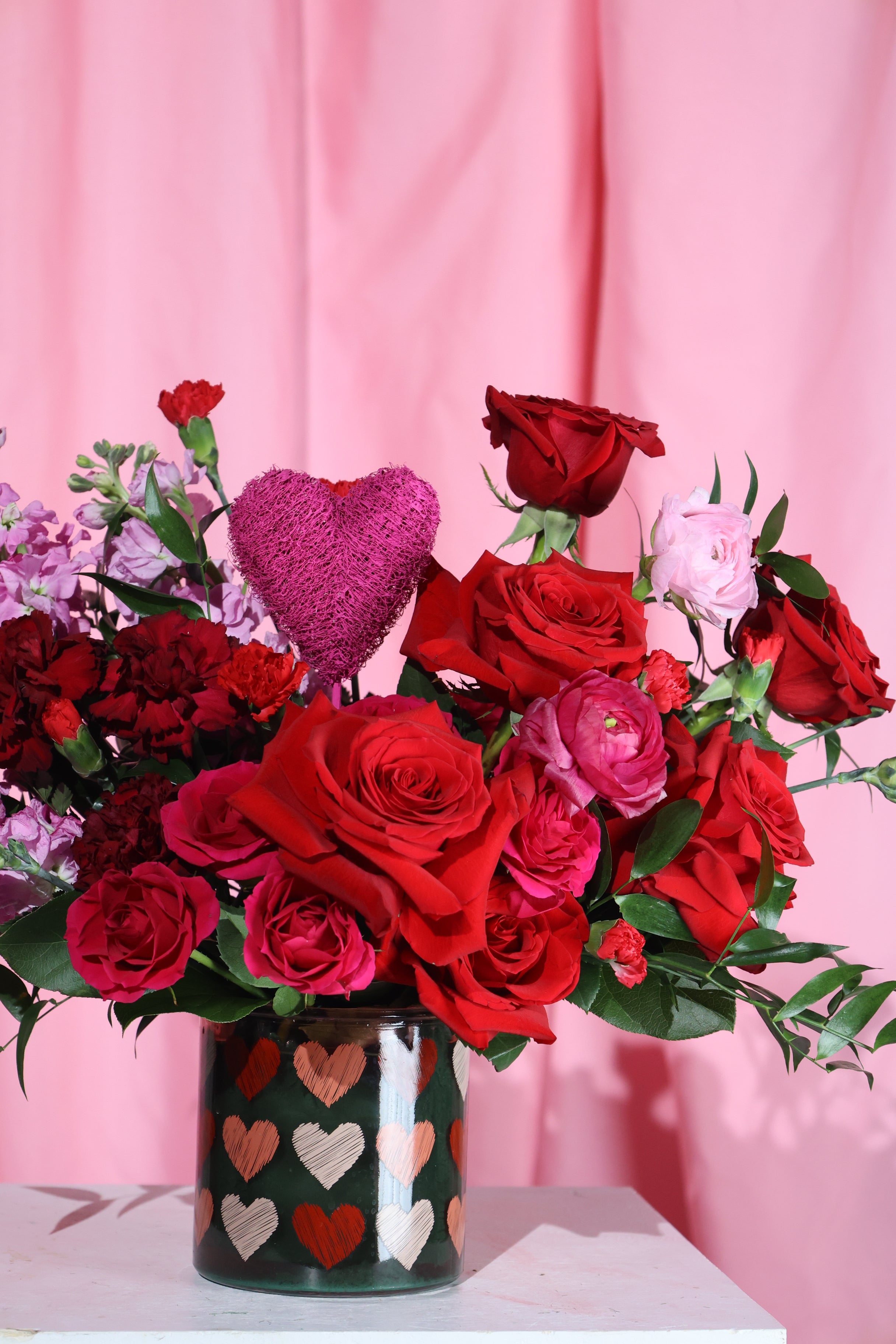 Bouquet of red and pink roses with a heart-shaped container on a pink background