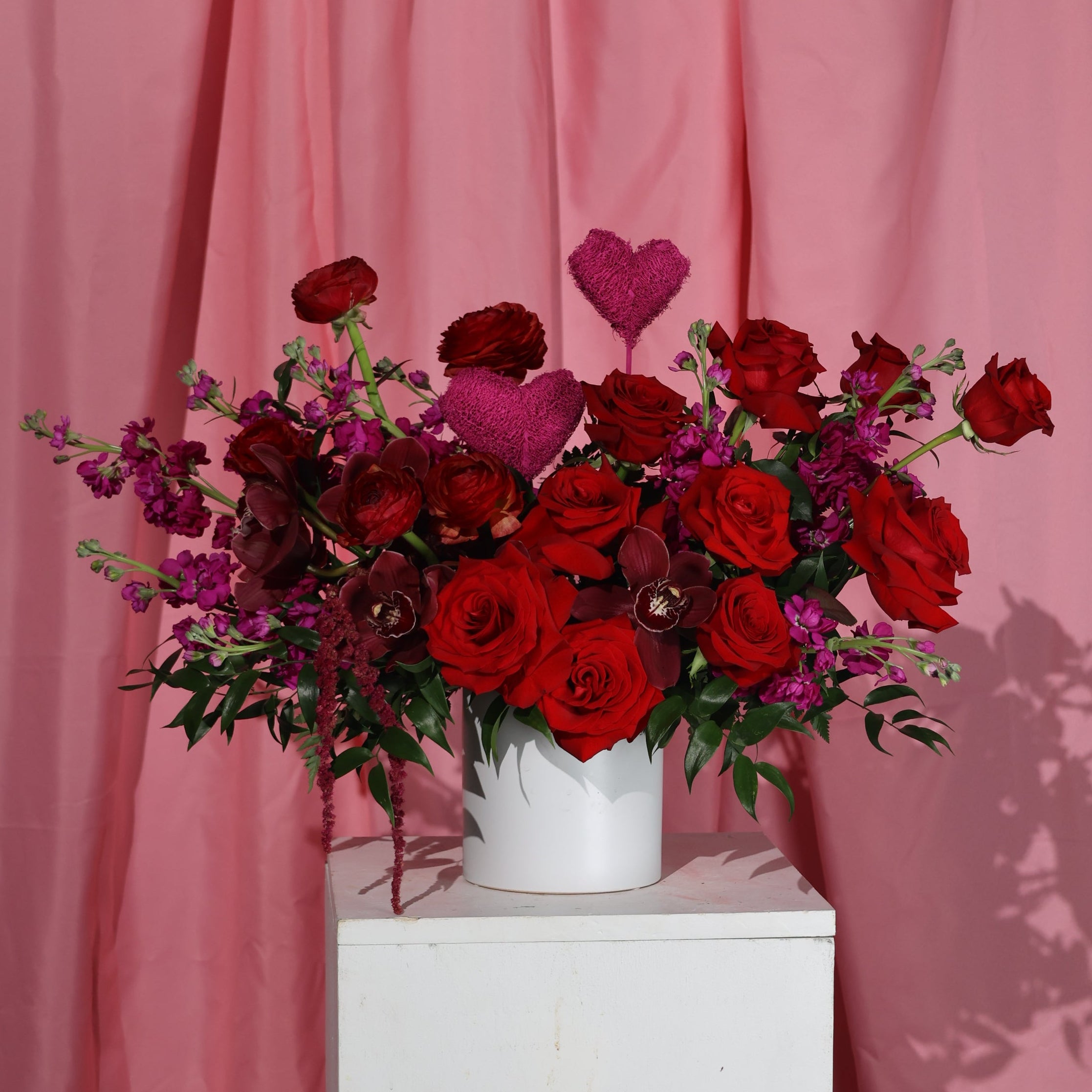 Bouquet of red roses and purple flowers on a pink background