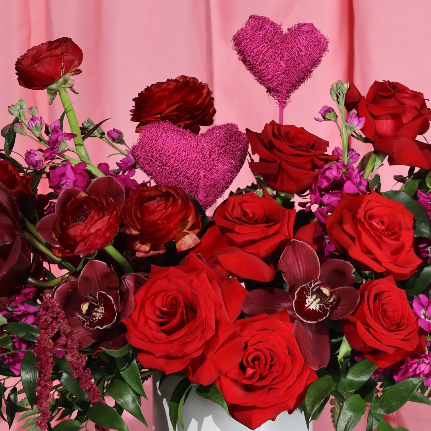 Bouquet of red roses and heart-shaped decorations on a pink background