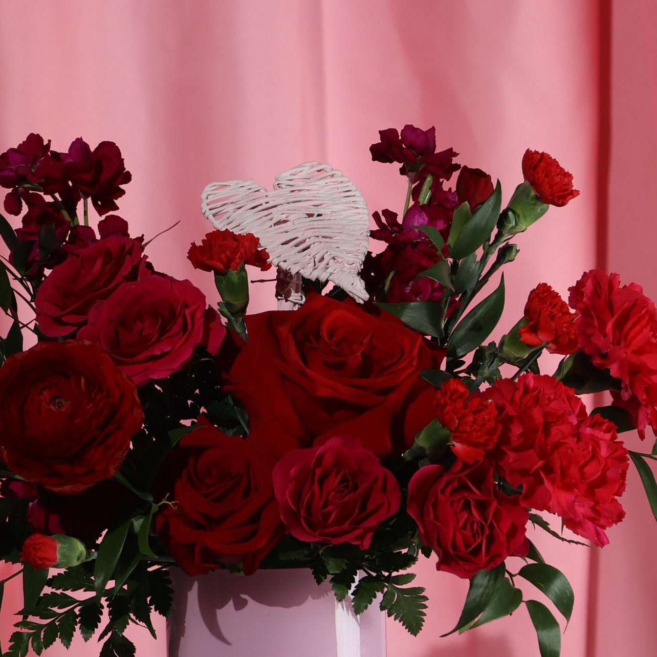 Bouquet of red flowers with a white heart against a pink background