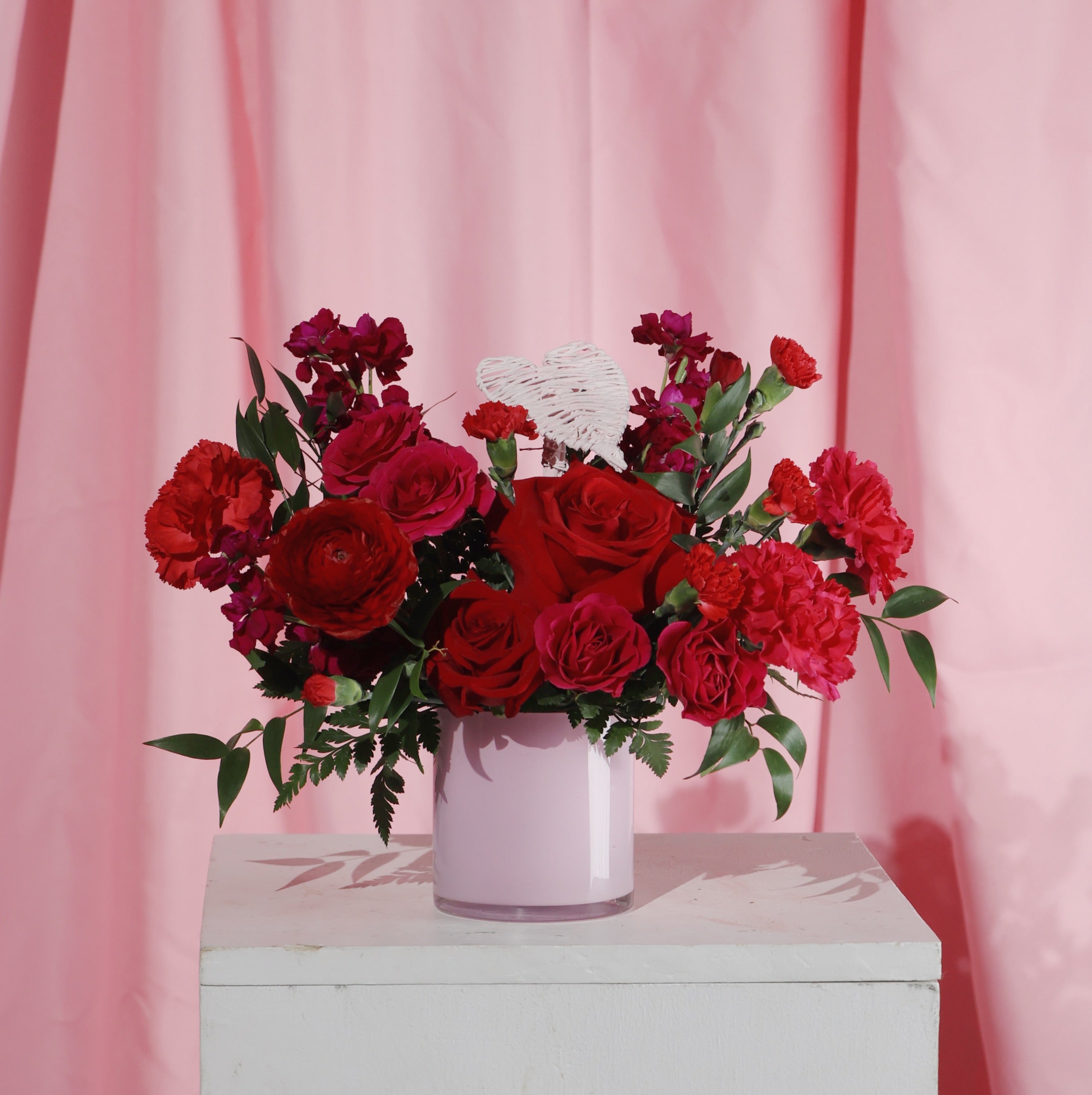 Bouquet of red roses in a pink vase against a pink curtain background